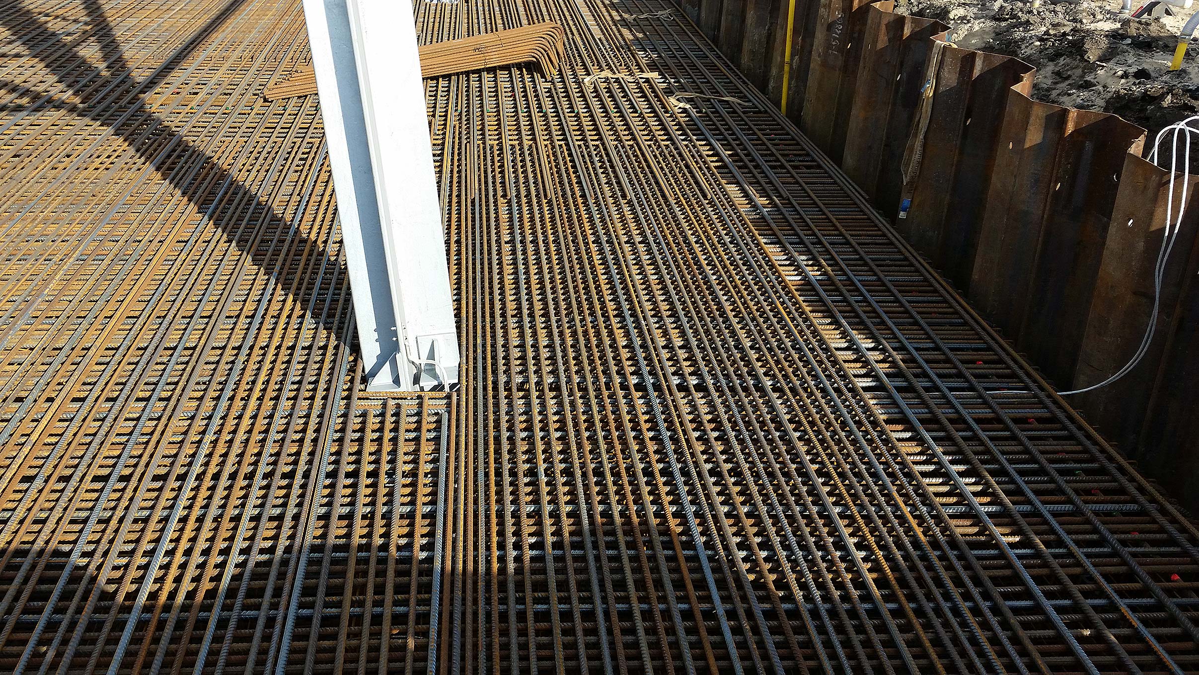 Projekte, die überzeugen Stahlbewehrung auf einer Baustelle, vorbereitet für Beton, mit einem weißen Stahlträger und Stahlbohlen im Hintergrund.